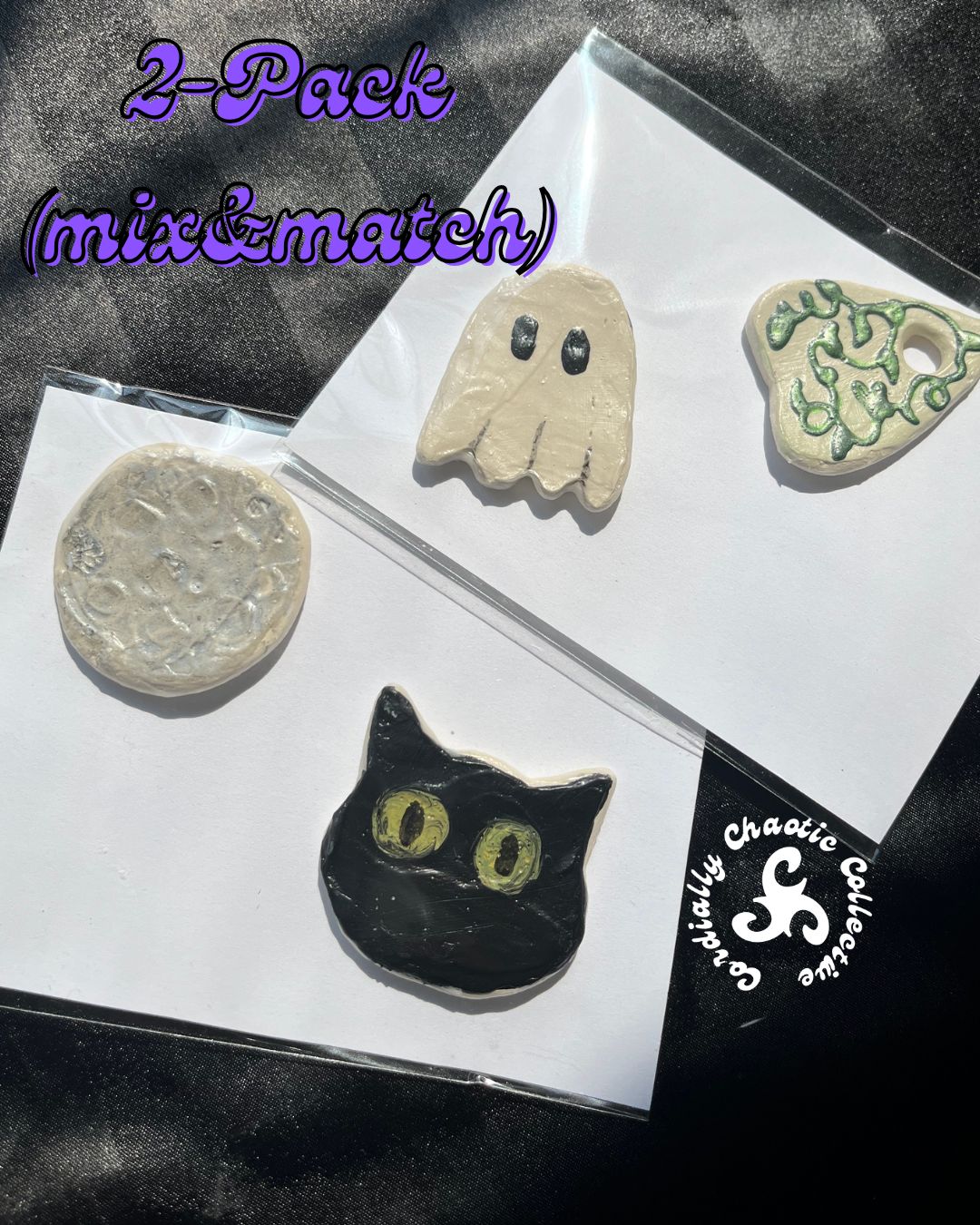 Two sets of two handcrafted Halloween-themed fridge magnets displayed on white backing cards over a black textured fabric background. The sets includes a black cat head with yellow eyes with a silver moon, and a beige ghost with a green ivy planchette.
